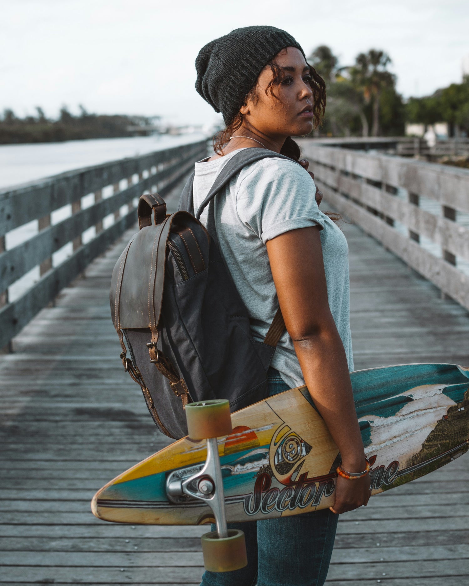 Lady with a Longboard and a Backpack by the Beach